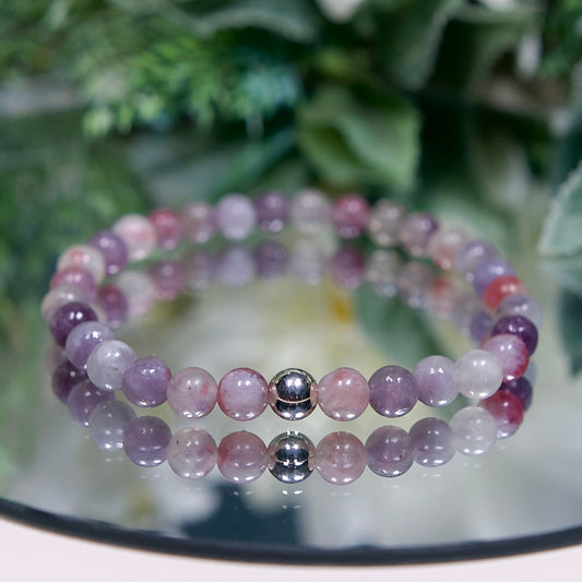 A multi-tonal pink and purple Lepidolite in Pink Tourmaline beaded gemstone bracelet with smooth round beads and a sterling silver accent bead on a mirrored plate