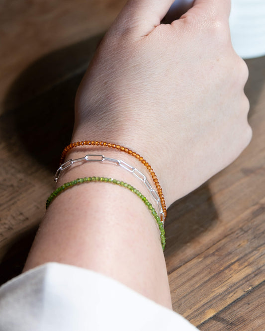 Dainty green chrome diopside beaded bracelet stacked on a wrist with orange citrine and sterling silver paperclip chain