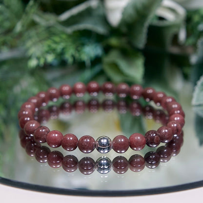 A muted burgundy Rose Jasper beaded gemstone bracelet with smooth round beads and a sterling silver accent bead on a mirrored plate