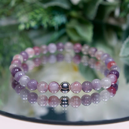 A multi-tonal pink and purple Lepidolite in Pink Tourmaline beaded gemstone bracelet with smooth round beads and a sterling silver accent bead on a mirrored plate