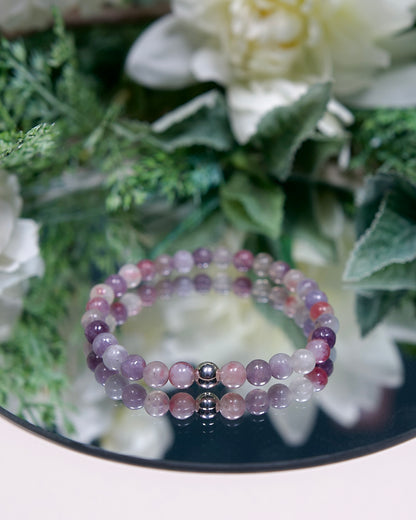 A multi-tonal pink and purple Lepidolite in Pink Tourmaline beaded gemstone bracelet with smooth round beads and a sterling silver accent bead on a mirrored plate