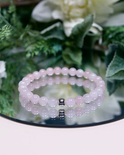 A pale opaque pink Madagascar Rose Quartz beaded gemstone bracelet with smooth round beads and a sterling silver accent bead on a mirrored plate