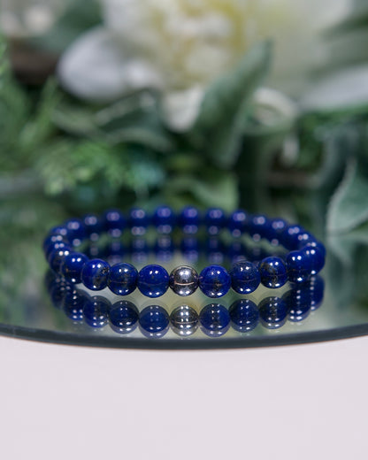 A deep rich blue Lapis Lazuli beaded gemstone bracelet with smooth round beads and a sterling silver accent bead on a mirrored plate