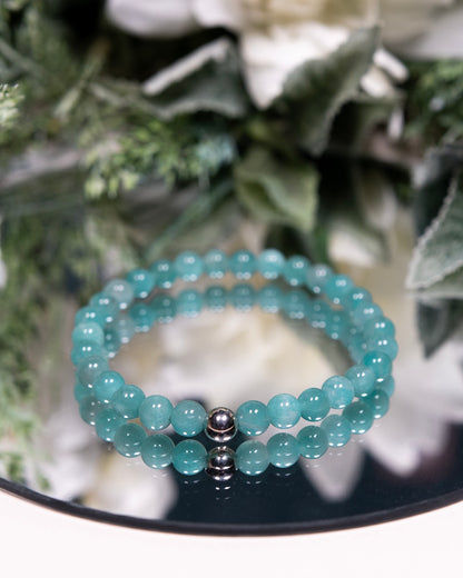 A turquoise Peruvian Amazonite beaded gemstone bracelet with smooth round beads and a sterling silver accent bead on a mirrored plate