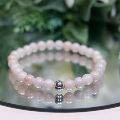 A pale pinkish-white Pink Opal beaded gemstone bracelet with smooth round beads and a sterling silver accent bead on a mirrored background