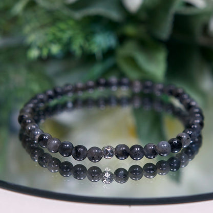 A marbled dark grey and black Larvikite beaded gemstone bracelet with smooth round beads and a hammered sterling silver accent bead on a mirrored plate