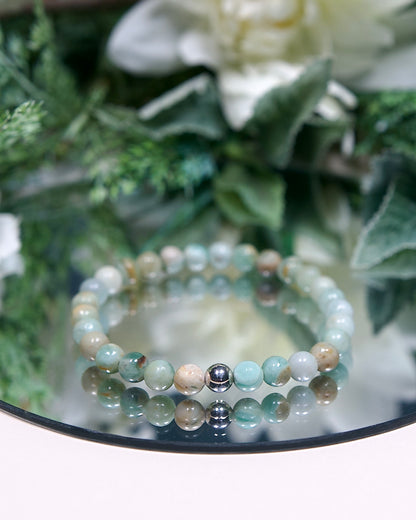 An Australian Agate beaded bracelet with round smooth pale mint green, tan, and white mottled beads and a sterling silver accent bead on a mirrored plate