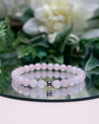 A pale opaque pink Madagascar Rose Quartz beaded gemstone bracelet with smooth round beads and a sterling silver accent bead on a mirrored plate