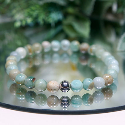 An Australian Agate beaded bracelet with round smooth pale mint green, tan, and white mottled beads and a sterling silver accent bead on a mirrored plate