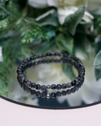 A marbled dark grey and black Larvikite beaded gemstone bracelet with smooth round beads and a hammered sterling silver accent bead on a mirrored plate