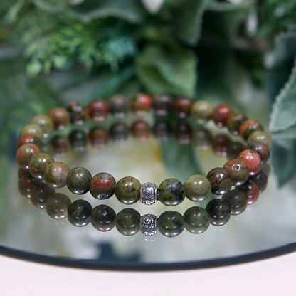 Close up photo of Unakite gemstone beaded A Unakite beaded gemstone bracelet with earthy green and pink smooth round beads and a sterling silver Tibetan accent bead on a mirrored plate with sterling silver accent