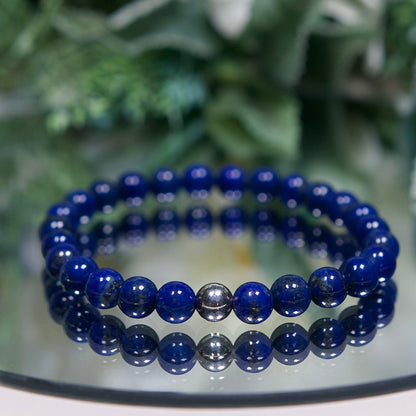 A deep rich blue Lapis Lazuli beaded gemstone bracelet with smooth round beads and a sterling silver accent bead on a mirrored plate