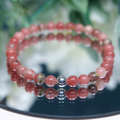 A Plum Blossom Jasper beaded gemstone bracelet with blush pink and green banded smooth round beads and a sterling silver accent bead on a mirrored plate