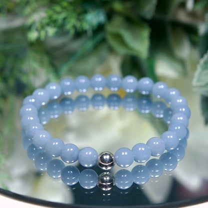 A powder blue beaded bracelet with smooth round Angelite gemstone beads and sterling silver accent bead on a mirrored plate