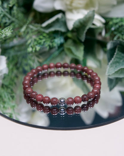 A muted burgundy Rose Jasper beaded gemstone bracelet with smooth round beads and a sterling silver accent bead on a mirrored plate