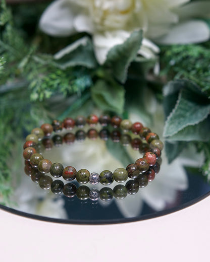 Close up photo of Unakite gemstone beaded A Unakite beaded gemstone bracelet with earthy green and pink smooth round beads and a sterling silver Tibetan accent bead on a mirrored plate with sterling silver accent