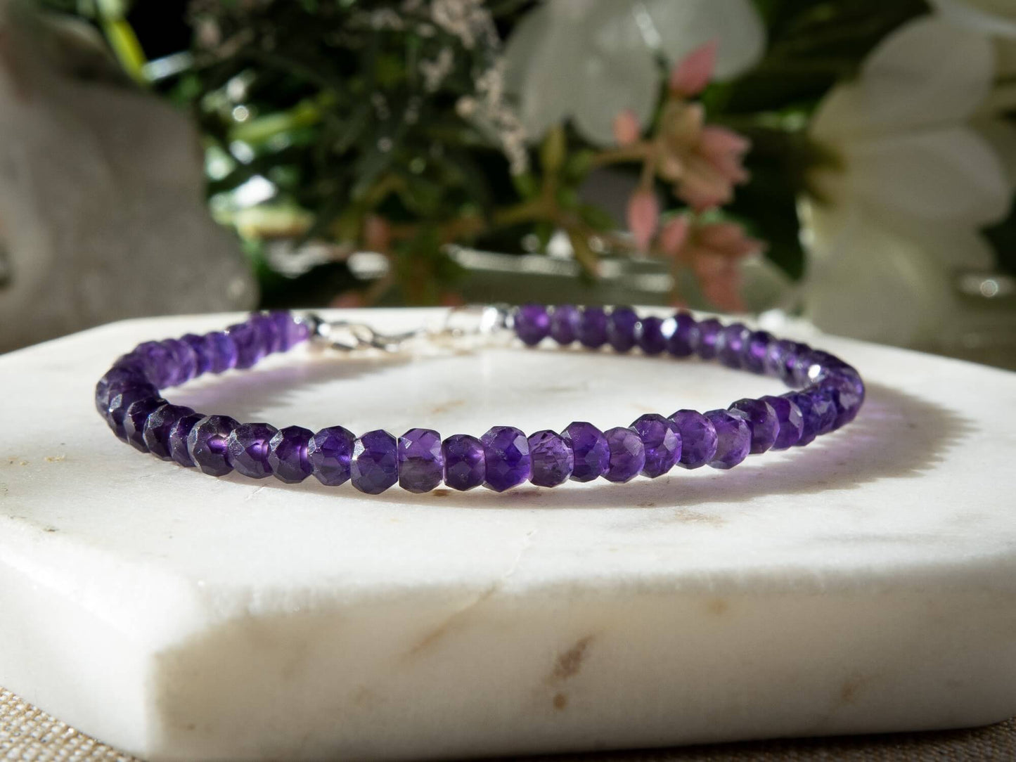 A faceted Amethyst beaded gemstone bracelet with a sterling silver spring ring clasp on a white coaster.