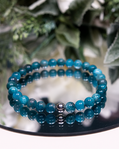 An Apatite beaded gemstone bracelet with round smooth bright teal beads and a sterling silver accent on a mirrored plate