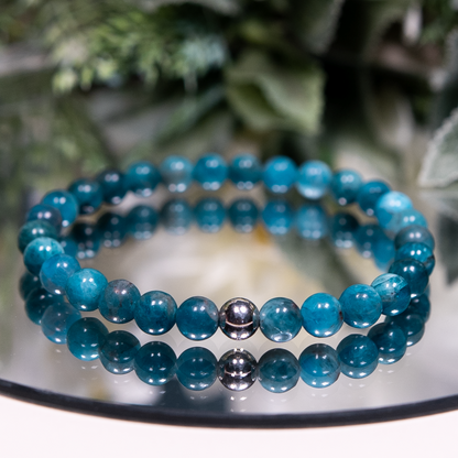 An Apatite beaded gemstone bracelet with round smooth bright teal beads and a sterling silver accent on a mirrored plate