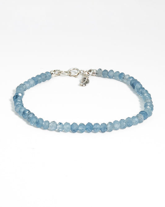 Top down photo of Aquamarine beaded gemstone bracelet with light and dark blue faceted roundelle shaped beads with sterling silver leaf-shaped charm and spring ring clasp
