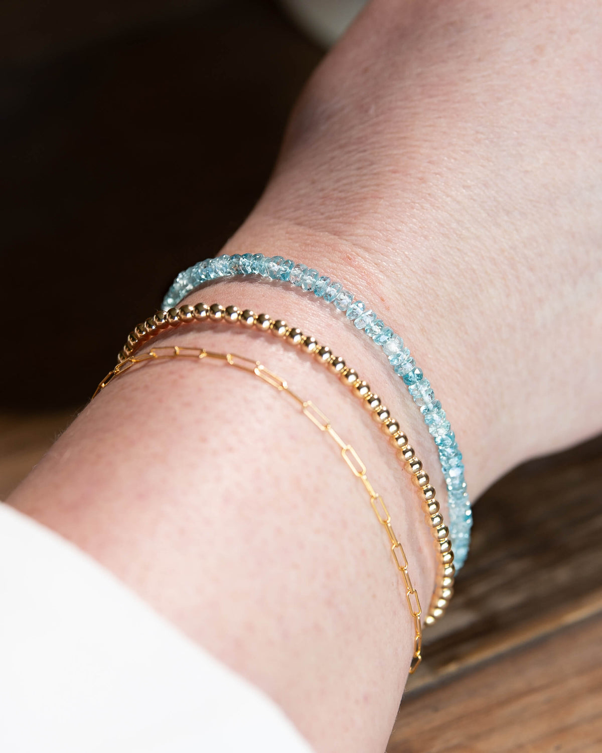 Pale blue Zircon beaded gemstone bracelet stacked on wrist with 14k gold-filled paperclip chain, and 14k gold-filled beaded bracelet.