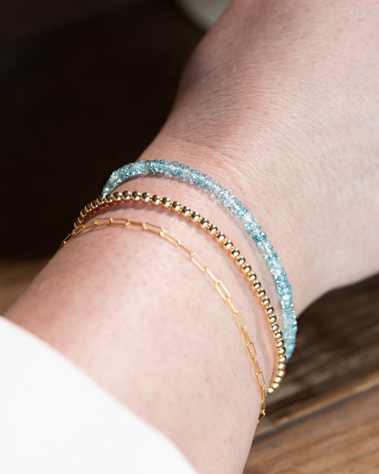 Pale blue Zircon beaded gemstone bracelet stacked on wrist with 14k gold-filled paperclip chain, and 14k gold-filled beaded bracelet.