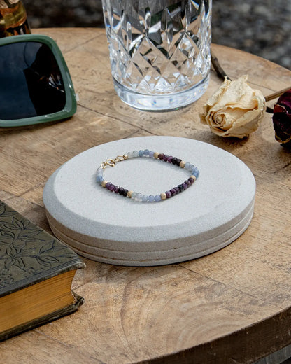 Light blue and dark purple faceted sapphire beaded bracelet with stardust 14k gold-filled accent beads and 14k gold-filled spring ring clasp on light coaster on wood table
