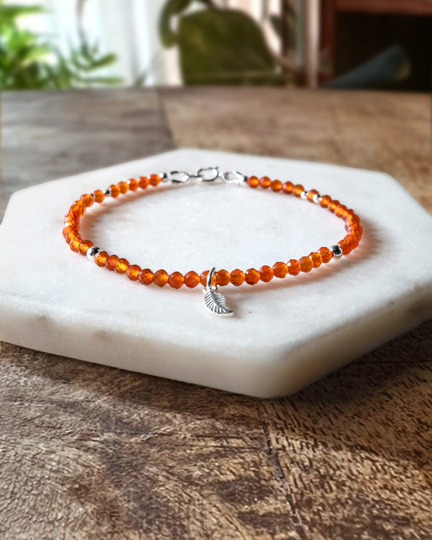 Orange carnelian gemstone beaded bracelet with sterling silver leaf-shaped charm and spring ring clasp.