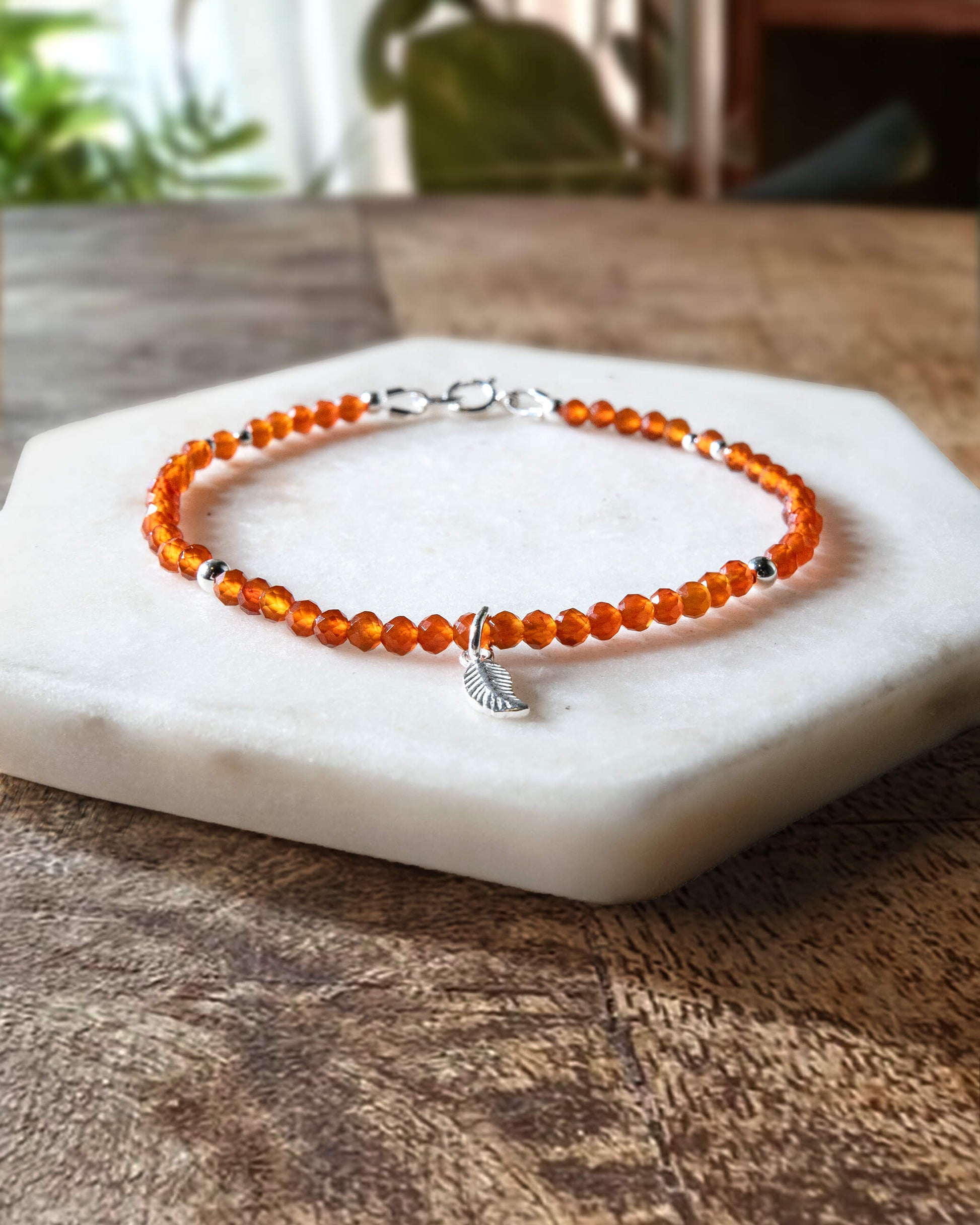 Orange carnelian gemstone beaded bracelet with sterling silver leaf-shaped charm and spring ring clasp.