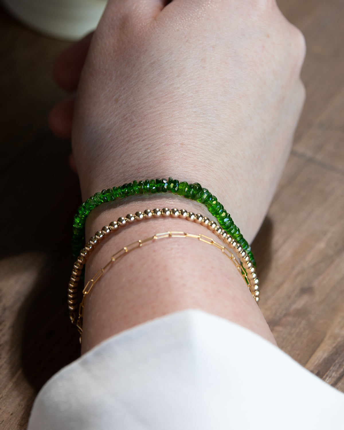 Bright green chrome diopside beaded gemstone bracelet stacked on a wrist with 14k gold-filled paperclip chain, and 14k gold-filled beaded bracelet.