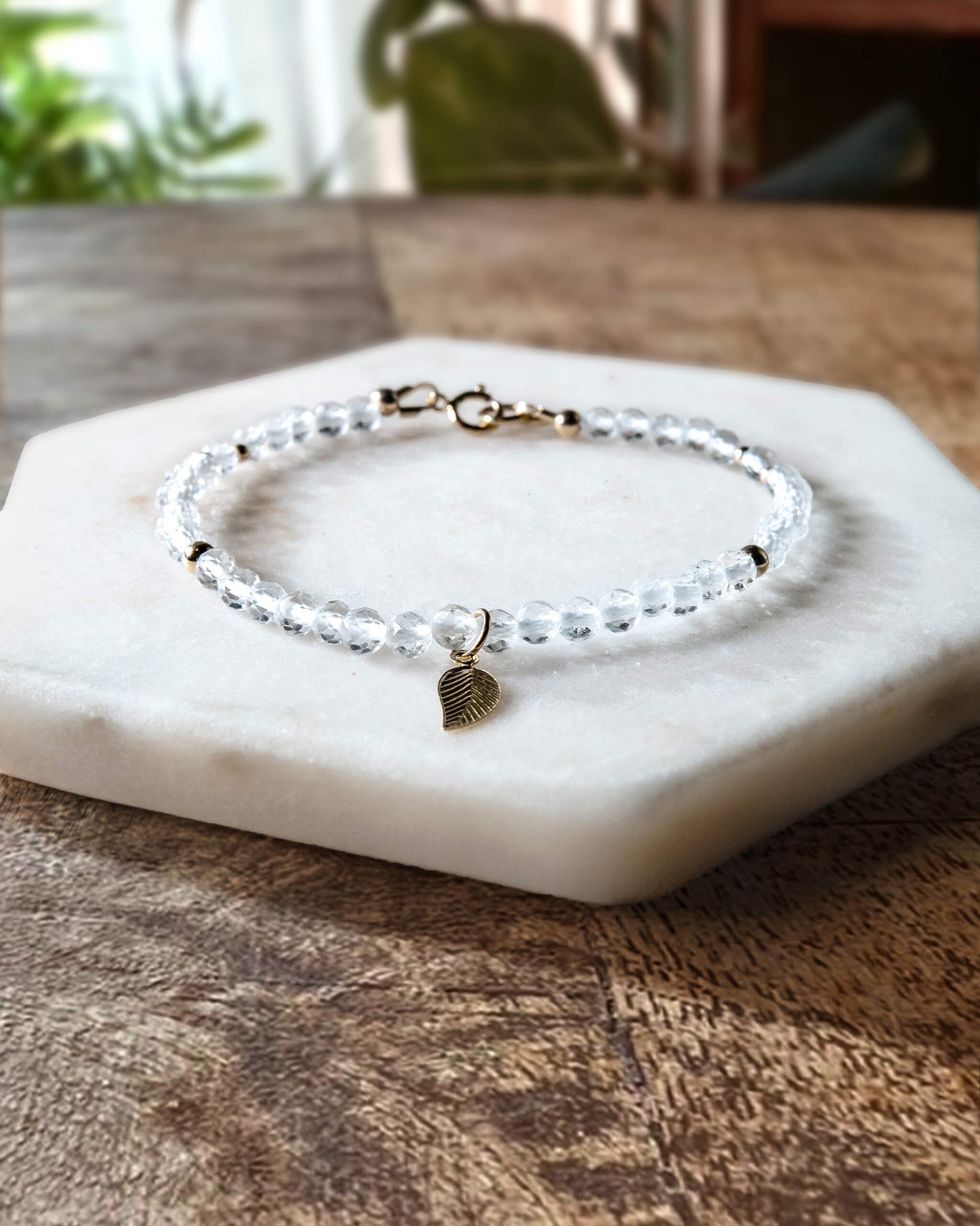 Clear quartz gemstone bracelet with 14k gold-filled leaf-shaped charm and spring ring clasp.