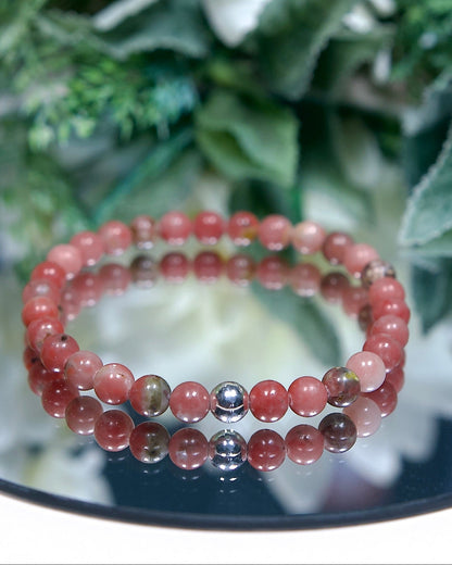 A Plum Blossom Jasper beaded gemstone bracelet with blush pink and green banded smooth round beads and a sterling silver accent bead on a mirrored plate
