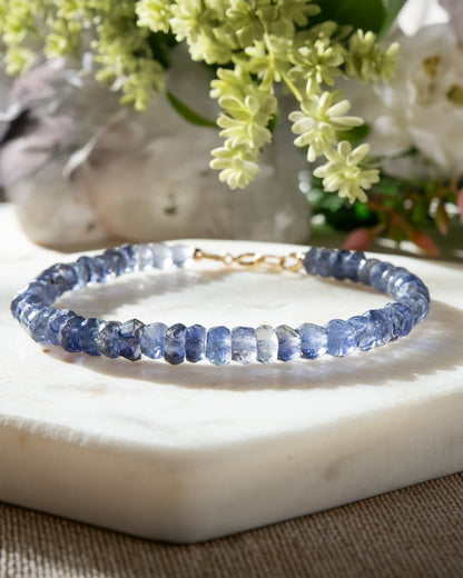 Dark blue, high clarity faceted Iolite beaded bracelet with 14k gold-filled spring ring clasp on white coaster on beige table