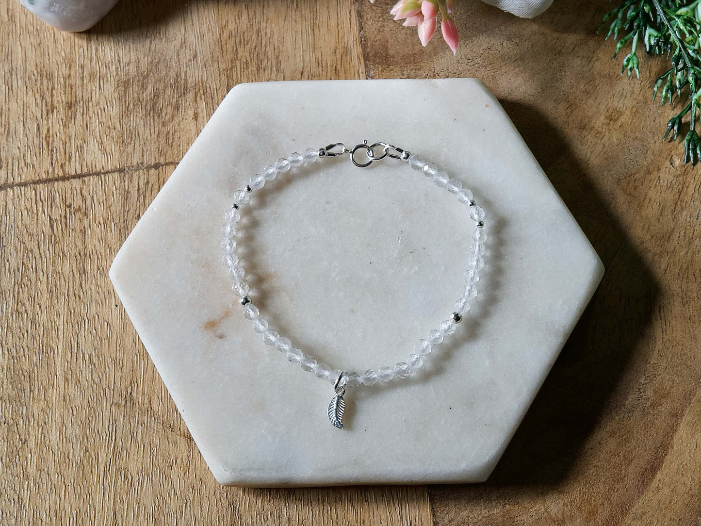 Clear quartz gemstone bracelet with sterling silver leaf-shaped charm and spring ring clasp.