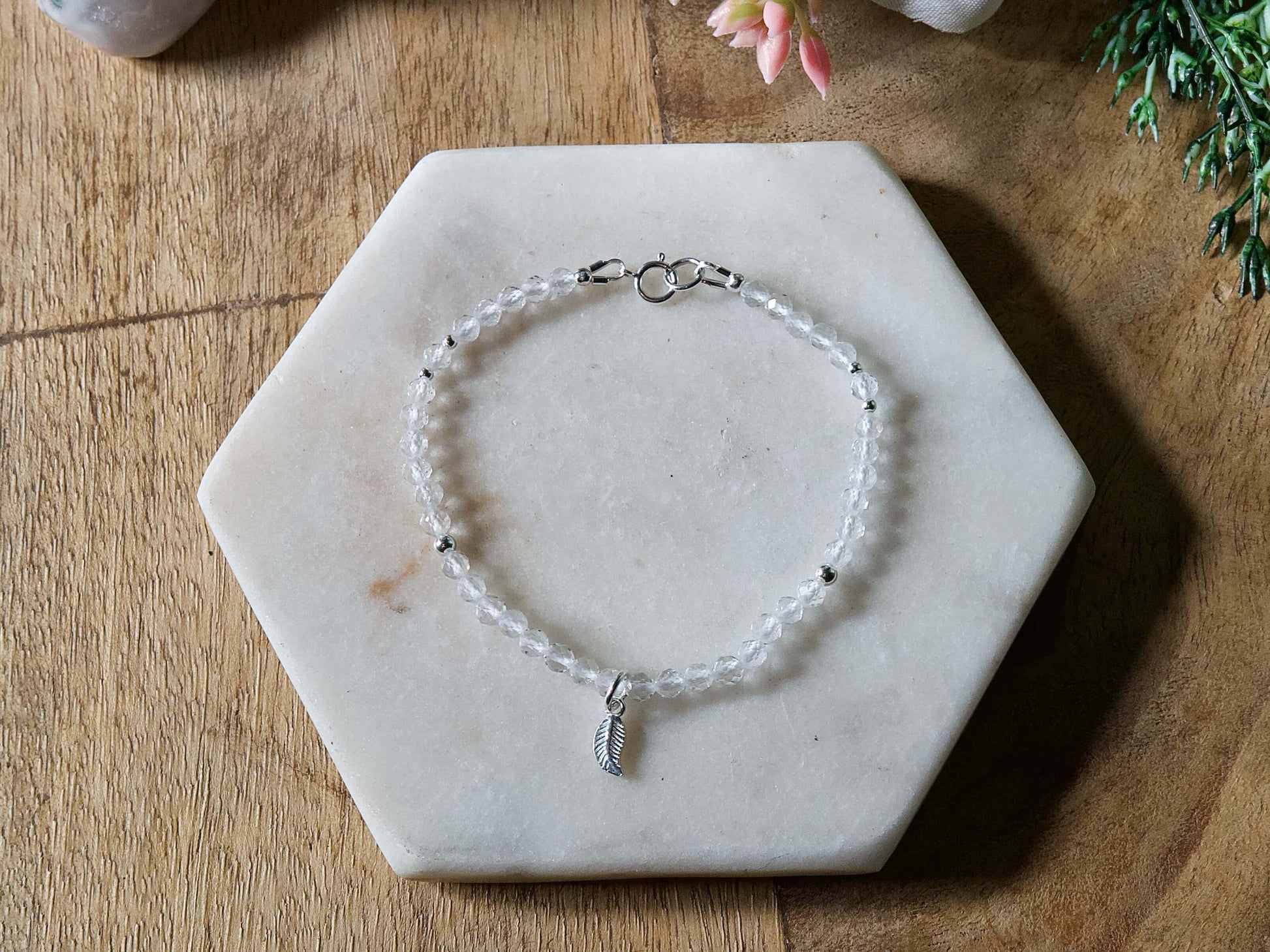 Clear quartz gemstone bracelet with sterling silver leaf-shaped charm and spring ring clasp.