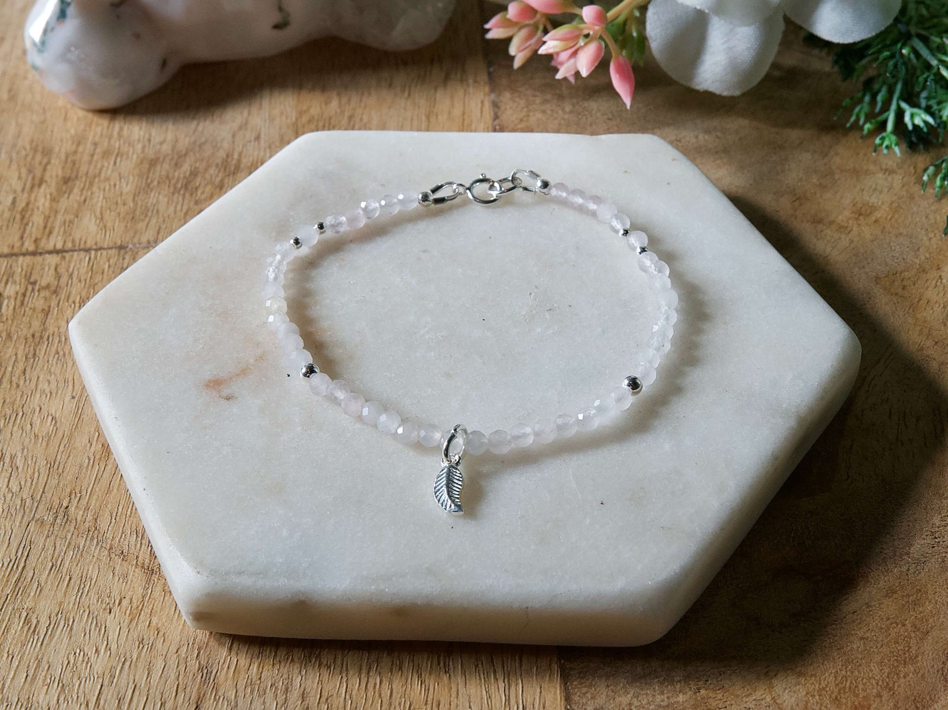 Pale pink rose quartz gemstone beaded bracelet with sterling silver leaf-shaped charm and spring ring closure.