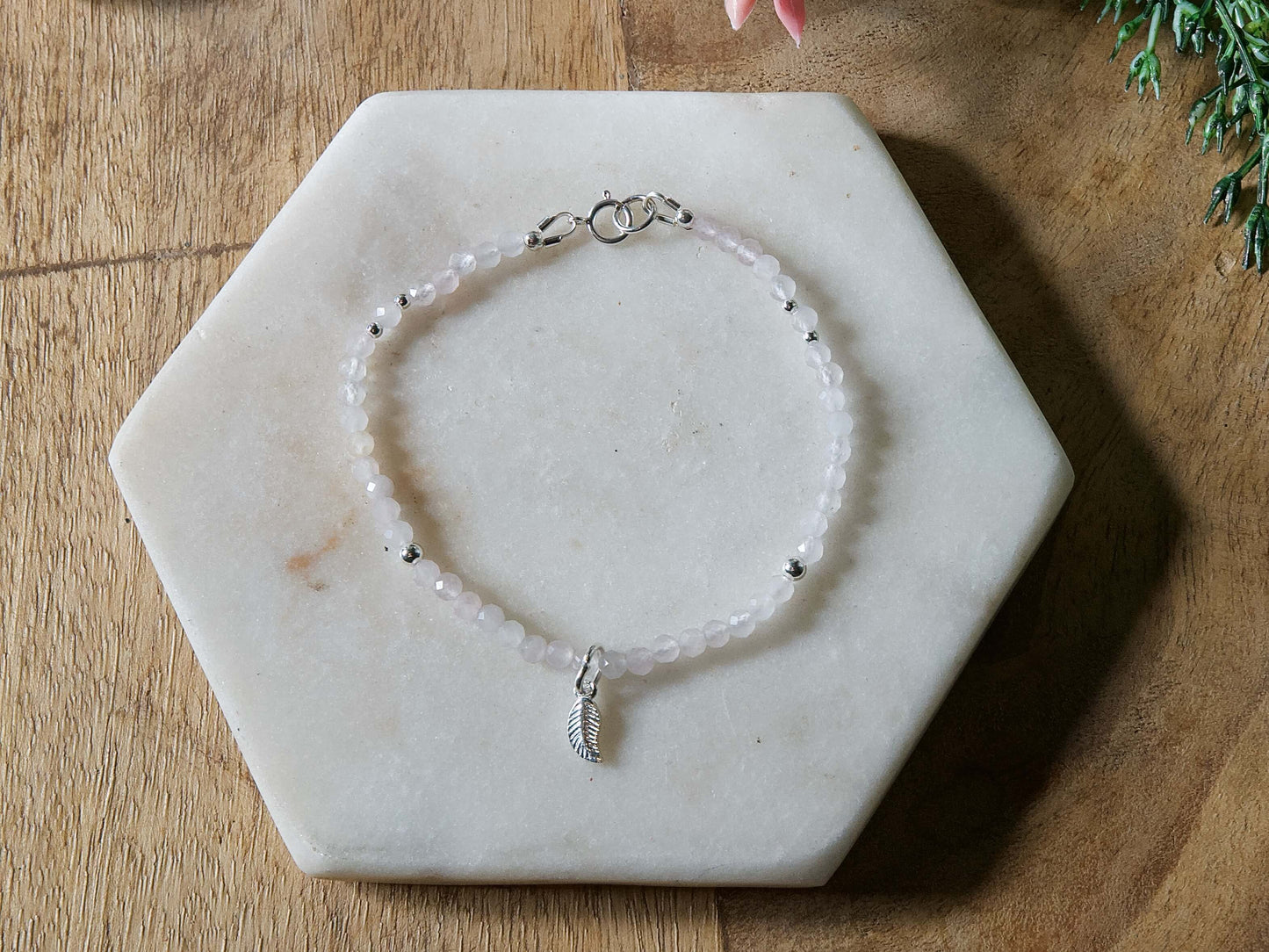 Pale pink rose quartz gemstone beaded bracelet with sterling silver leaf-shaped charm and spring ring closure.