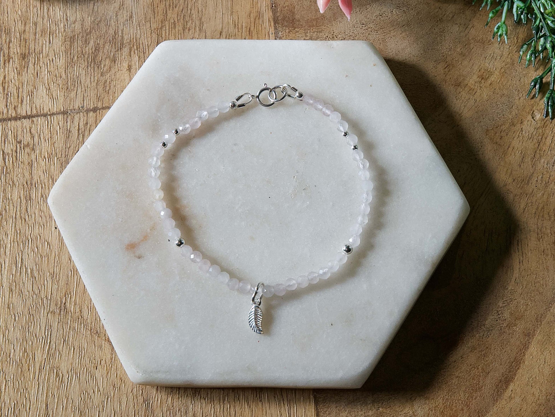 Pale pink rose quartz gemstone beaded bracelet with sterling silver leaf-shaped charm and spring ring closure.