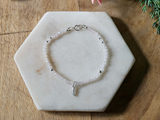 Pale pink rose quartz gemstone beaded bracelet with sterling silver leaf-shaped charm and spring ring closure.