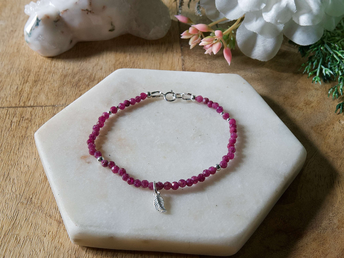 Deep pink ruby gemstone beaded bracelet with sterling silver leaf-shaped charm and spring ring closure.