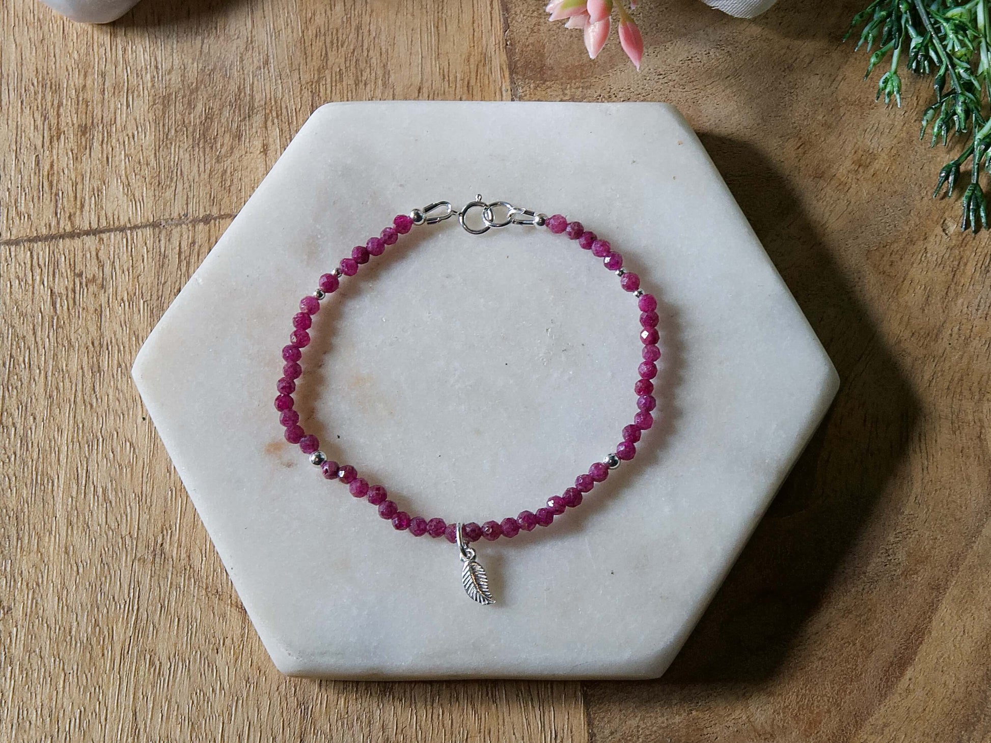 Deep pink ruby gemstone beaded bracelet with sterling silver leaf-shaped charm and spring ring closure.