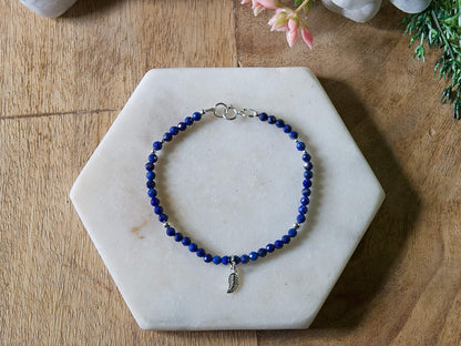 Deep blue lapis lazuli gemstone beaded bracelet with sterling silver leaf-shaped charm and spring ring clasp.