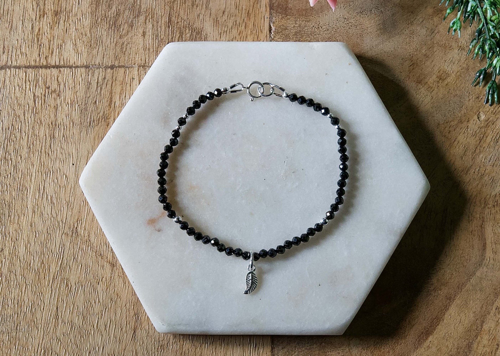 Black onyx gemstone beaded bracelet with sterling silver leaf-shaped charm and spring ring closure.