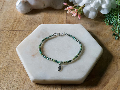 Turquoise and black African turquoise gemstone beaded bracelet with sterling silver leaf-shaped charm and spring ring clasp.