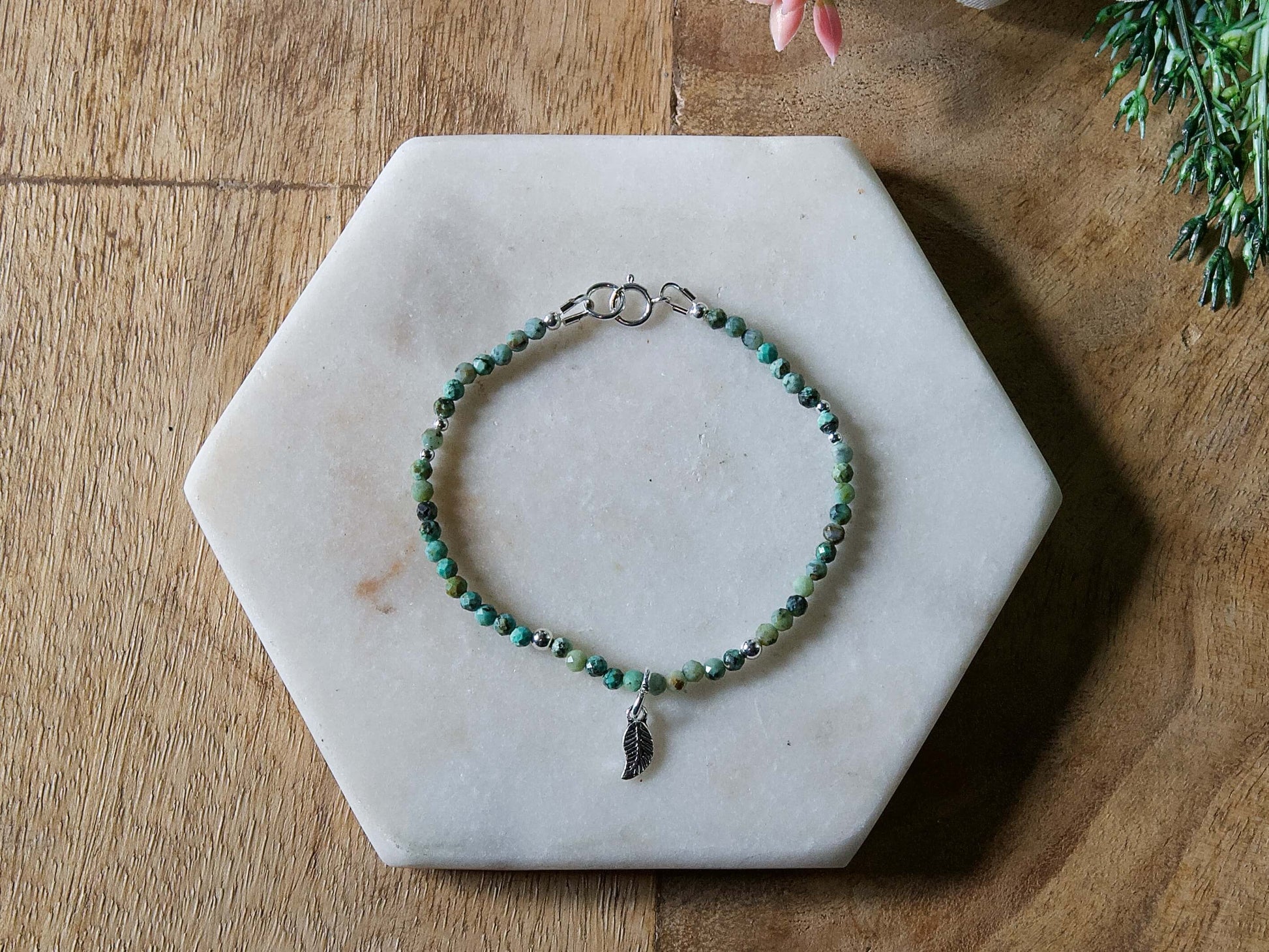 Turquoise and black African turquoise gemstone beaded bracelet with sterling silver leaf-shaped charm and spring ring clasp.