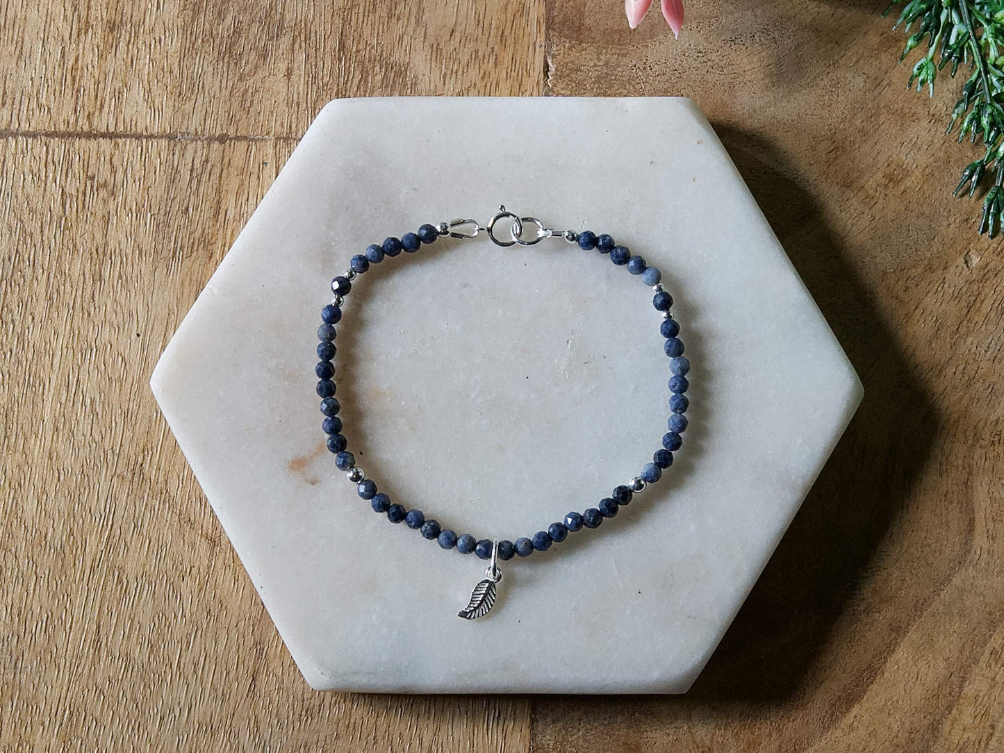 Deep blue sapphire gemstone beaded bracelet with sterling silver leaf-shaped charm and spring ring closure.