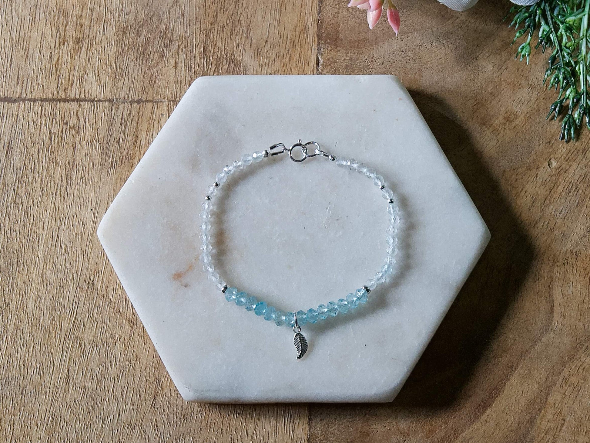 Blue and white topaz gemstone beaded bracelet with sterling silver leaf-shaped charm and spring ring clasp.
