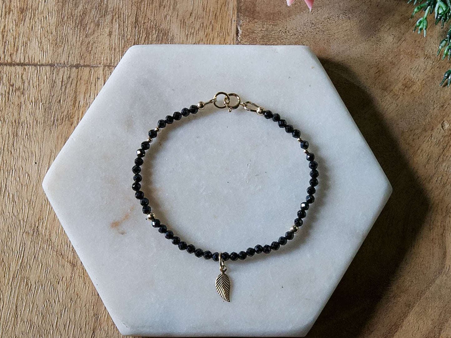 Black spinel gemstone beaded bracelet with 14k gold-filled leaf-shaped charm and spring ring clasp.