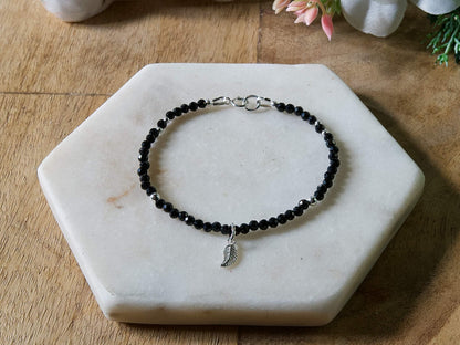 Black spinel gemstone beaded bracelet with sterling silver leaf-shaped charm and spring ring clasp.