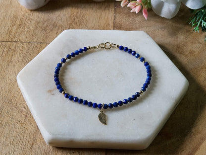 Deep blue lapis lazuli gemstone beaded bracelet with 14k gold-filled leaf-shaped charm and spring ring clasp.